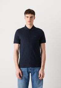 Námornícky polo tričko s zipsovým golierom, krátkymi rukávmi a malou nášivkou loga, vyrobené z hladkého materiálu s priliehavým strihom.