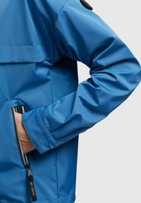 Blue waterproof jacket featuring a high collar, zippered pocket, and adjustable cuff with a sleek, smooth texture.