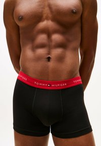 Schwarze Baumwoll-Boxershorts mit einem roten Bündchen, das das Logo "TOMMY HILFIGER" trägt; enganliegendes Design mit glatter Textur.