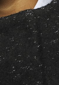 Svart stickad tröja i närbild, med en texturerad yta som har små vita fläckar och ett mjukt, luddigt utseende.