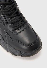 Nærbilde av svart chunky sneakers med tykke snorer, teksturert såle og "GUESS"-logo på siden.