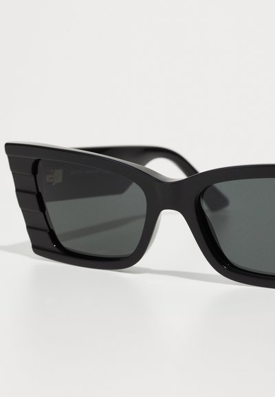 Black sunglasses with a geometric design, flat top, and pronounced side accents. Gray lenses offer a sleek, modern appearance.