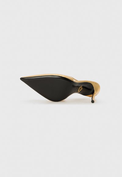 Zapato stiletto dorado y negro con punta afilada, parte superior texturizada y tacón negro delgado. Diseño limpio y minimalista.