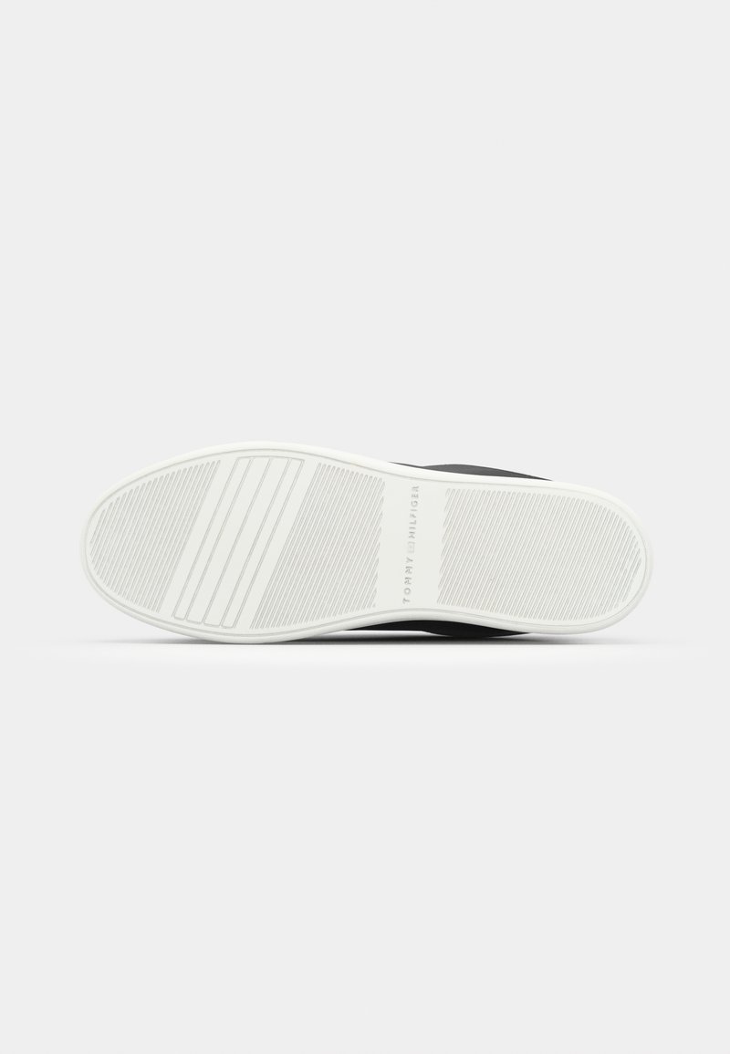 Zapatilla negra con un upper texturizado y una suela de goma blanca que presenta surcos horizontales y una marca en el lateral.