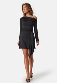 Zwarte off-shoulder jurk met lange mouwen, aansluitende bustier, gedrapeerde rok en bloemdessin op de schouder. Soepele, rekbare stof.