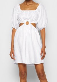 Valkoinen puffihihainen mekko, jossa on neliönmuotoinen pääntie ja uurretyksellä varustettu leikkaus, jossa on pyöreä detalji vyötäröllä. Valmistettu kevyestä kankaasta.