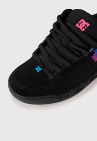 Black sneaker featuring a smooth texture, perforated details, prominent laces, and a blue DC logo with pink and purple accents on the side.