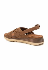 Sandalias de cuero marrón con patrones de flores perforados, correa en el tobillo ajustable, suela de color claro y un leve tacón tipo cuña.