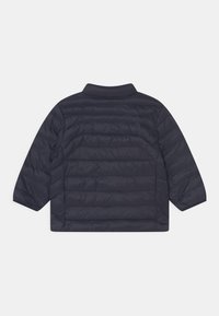 Prošívaná tmavě modrá bunda s límečkem a krátkými rukávy. Má horizontální prošívání a hladkou, lesklou texturu látky.