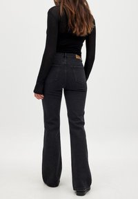 Črne široke jeans hlače z visokim pasom, z usnjenim označevalcem na hrbtni strani, stranskimi žepi in gladko denimsko teksturo.