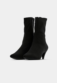 Μαύρα μποτάκια αστραγάλου με μυτερή σχεδίαση, κατασκευασμένα από μαλακό υλικό. Διαθέτουν πλ ευρικό φερμουάρ και λεπτό τακούνι. Λείο υλικό, χωρίς ορατά σχέδια.