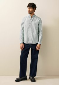 Lyseblå stribet skjorte med knapper lavet af åndbart stof, parret med mørke denimbukser og sorte klodsede loafers.