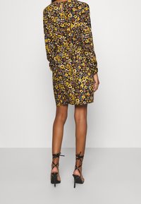 Robe à motifs floraux avec manches longues, taille élastique et ouverture au dos en forme de trou de serrure. Associée à des sandales noires à talons hauts et à lanières.