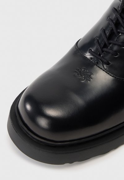 Schwarzer Lederstiefel mit glänzender Oberfläche, runder Zehenform und schwarzen Schnürsenkeln. Verfügt über eine strukturierte Sohle und ein geprägtes Logo-Detail an der Seite.
