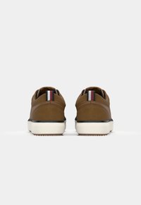 Paire de chaussures marron décontractées vues de dos avec des languettes rayées blanches, rouges et bleues et des semelles en caoutchouc blanches.
