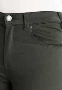 Olijfgrijze denim jeans met een gladde textuur, voorzien van een metalen knoopsluiting en een enkele voorzak.