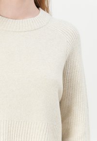 Maglione lavorato a maglia color crema con scollo rotondo a costine, corpo testurizzato e orlo a costine. Design semplice con vestibilità rilassata.