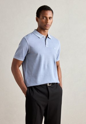 Light blue short-sleeve polo shirt featuring a collar and a small embroidered logo. Paired with black trousers, showcasing a classic design.