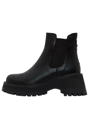 Bottines noires à talons épais portées avec des collants noirs transparents à pois et une jupe midi bleu vif sur fond blanc.