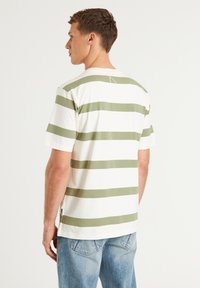 Dryžuota medvilninė marškinėliai su plačiais alyvų žaliais ir baltais dryžiais, trumpomis rankovėmis, apvalia apykakle ir šoniniu siūlų logotipu.