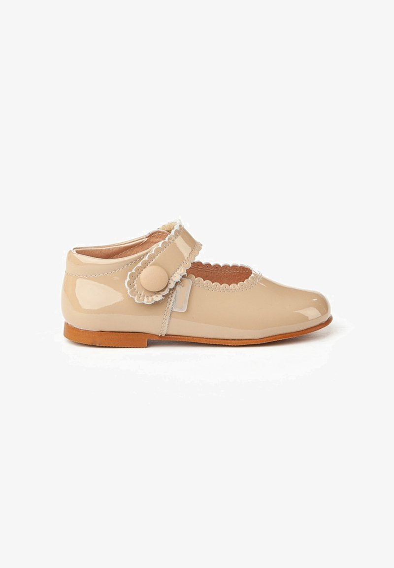 Zapato Mary Jane de charol beige con ribete ondulado y cierre de botón redondo. Punta redondeada y suela baja de goma marrón.