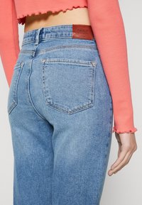 Jeans de mezclilla de tiro alto en azul claro con una etiqueta de cuero que dice "ONLY", que cuentan con dos bolsillos traseros y detalles de costura sutil.