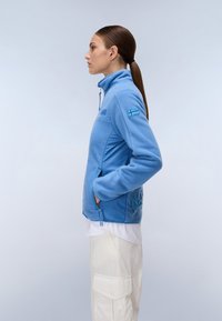 Giacca in fleece azzurro chiaro con colletto alto, tasche laterali e un pannello testurizzato con lettering in rilievo sul retro.