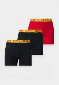 Τρία ανδρικά boxer briefs, δύο μαύρα και ένα κόκκινο, καθένα με κίτρινη μέση που έχει κόκκινο κείμενο "BJÖRN BORG SPAIN."