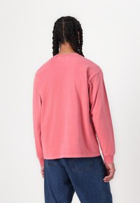 Pink long-sleeve shirt made of cotton with a rounded neckline. Features a relaxed fit and wrist cuffs. Back view shows stitching details.