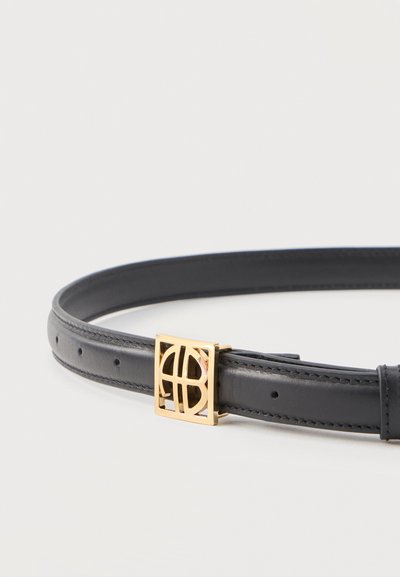 Juodas odinis diržas su auksine kvadrato formos sagtimi, kurioje yra geometrinis išpjovos dizainas, išdėliotas plokščiai ant balto paviršiaus.