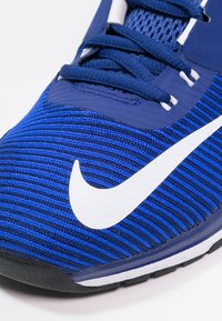 Sportovní obuv Nike v modré barvě s textilním svrškem, bílým logem swoosh a černou podrážkou. Obsahuje kontrastní modré šněrování a síťovinové detaily.