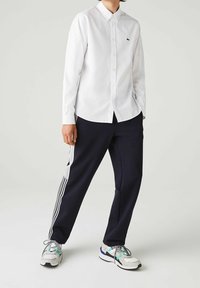 White button-up shirt with collar, black and white striped navy trousers, and multicolored sneakers. Smooth texture, casual fit.