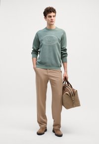 Felpa verde menta con logo in rilievo, pantaloni beige e borsa in pelle marrone coordinata. Tessuto liscia, vestibilità sportiva e dettagli discreti.