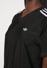 T-shirt sportif noir avec un col en V, des manches courtes et des accents blancs à trois bandes. Présente un petit logo blanc sur le côté gauche de la poitrine.