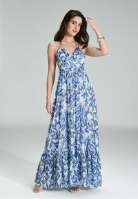 Robe maxi avec encolure halter, arborant des motifs paisley bleus sur fond blanc et un ourlet volanté. Tissu léger et fluide.