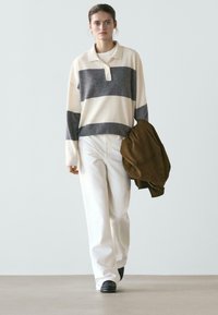 Pasiasta dzianinowa koszulka polo w kolorze kremowym i szarym, z guzikami przy kołnierzu; zestawiona z białymi spodniami o szerokich nogawkach i brązową kurtką. Czarne buty.