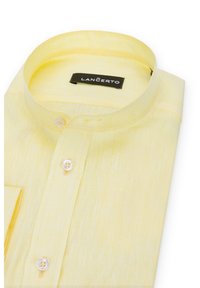 Żółta koszula z kołnierzykiem, wykonana z teksturowanej tkaniny, z połową guzików z przodu i kieszonką na lewej piersi. Metka widoczna wewnątrz kołnierza.