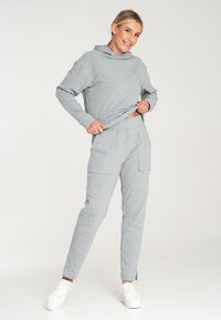 Jasnoszara bluza z kapturem i długimi rękawami, zestawiona z dopasowanymi dresami zwężającymi się ku dołowi, które mają boczne kieszenie.