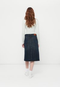 Mørkeblå denimskjørt med rett snitt, baklommer og en brun lærpatch i midjen. Hvit langermet topp brukt.