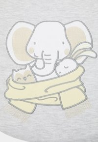 Grått stoff har et brodert design av en elefant som holder en kanin og en ugle, innhyllet i et gult skjerf med detaljerte frynser.