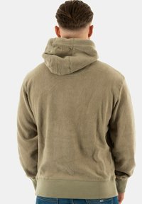 Sudadera de forro polar beige con capucha, puños y dobladillo acanalados. Superficie texturizada con un acabado suave. Diseño simple, sin logotipos ni acentos visibles.