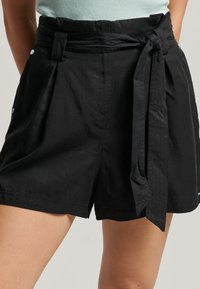 Pantaloni corti neri realizzati in tessuto leggero, dotati di una vita alta, cintura da annodare, parte anteriore plissettata e tasche laterali.