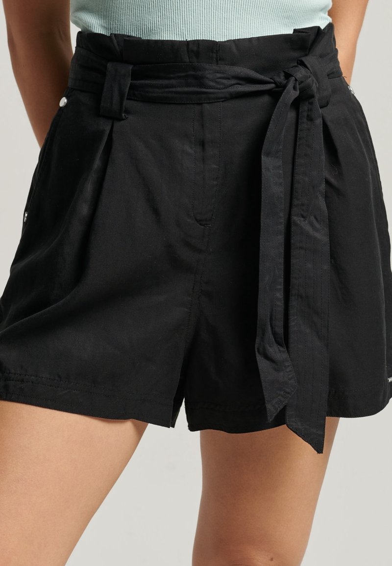 Pantaloni corti neri realizzati in tessuto leggero, dotati di una vita alta, cintura da annodare, parte anteriore plissettata e tasche laterali.