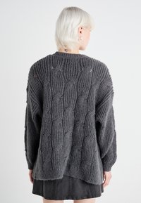 Kuscheliger grauer Strickpullover mit einem gerippten Muster, weiten Ärmeln und einem lockeren Schnitt mit einem leicht längeren Rückensaum.