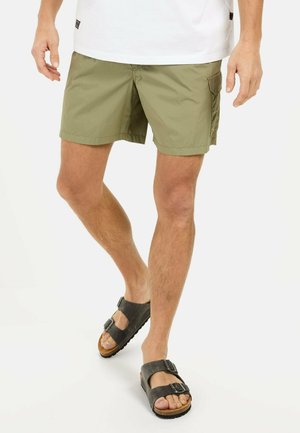 Olive green swim shorts with a smooth texture, two pockets, and a relaxed fit. Paired with black leather sandals featuring buckles.