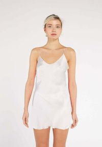 Silk camisole in light cream with a v-neck, thin spaghetti straps, and a gently curved hem, featuring a smooth, shiny texture.