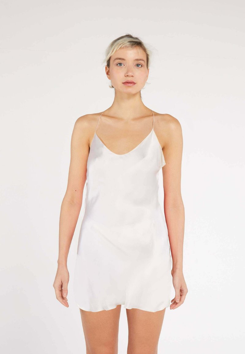 Silk camisole in light cream with a v-neck, thin spaghetti straps, and a gently curved hem, featuring a smooth, shiny texture.