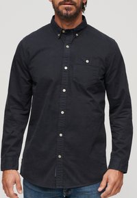 Marine blauwe button-up shirt met lange mouwen, een puntige kraag, een enkele borstzak en lichtgekleurde knopen. Gladde katoen textuur.