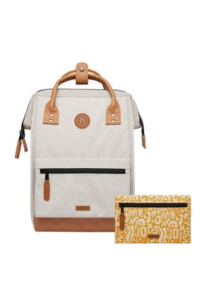 Beige fabric backpack with brown leather accents, featuring a front zip pocket, top handle, and an accompanying yellow patterned pouch.
