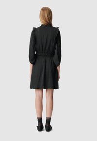 Abito nero con vita aderente, maniche lunghe a palloncino e scollatura arricciata. Tessuto leggero e morbido. Indossato con calze nere trasparenti e scarpe.